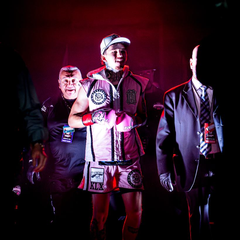 Fighter walking out in a pink and white robe flanked by his corner