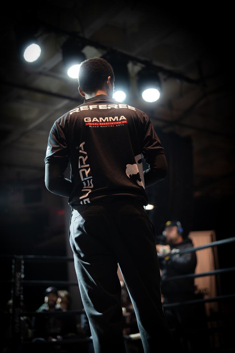 Crew member in a referee jacket leaning against the ropes