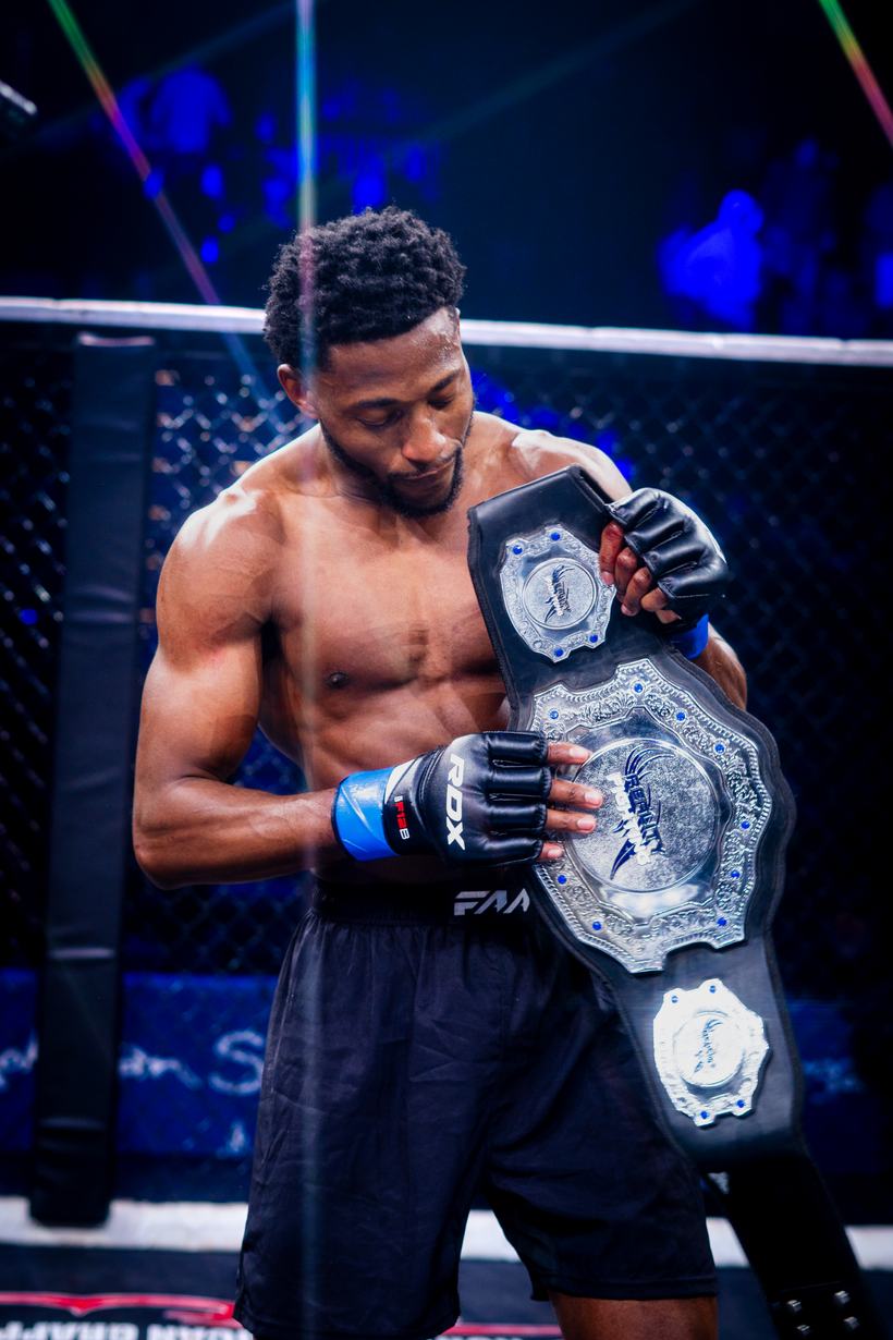 Champion holding two belts across his chest in the cage