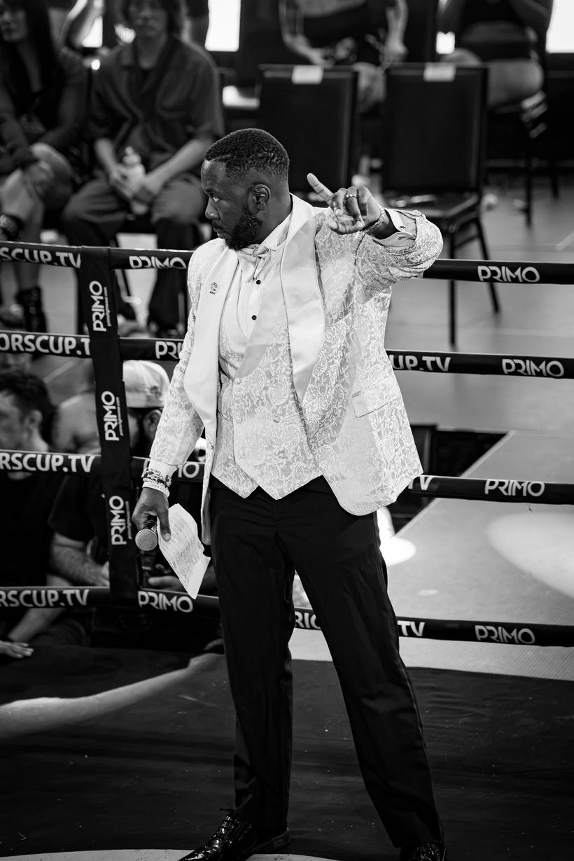 Announcer in a white dinner jacket pointing across the ring