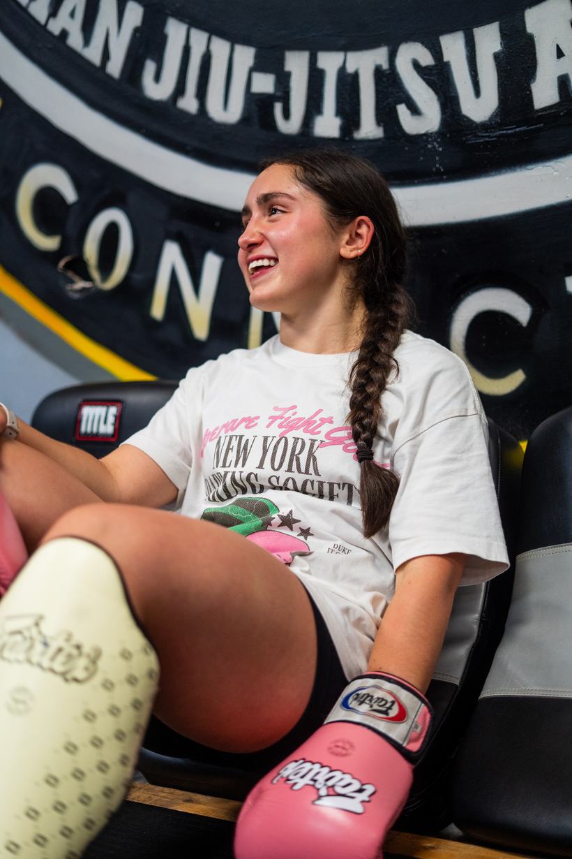 Young fighter laughing, pink gloves resting on her knee