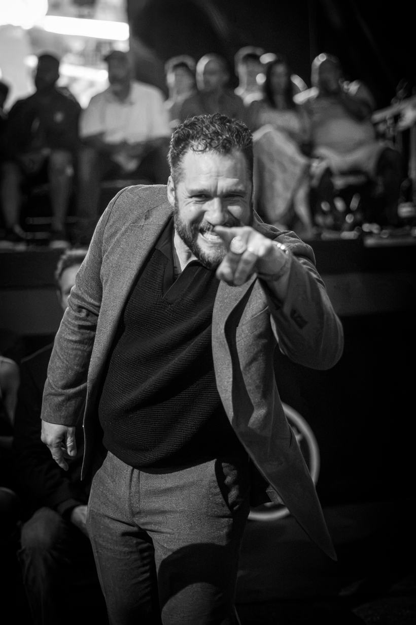 Bearded host pointing and laughing with the crowd behind him