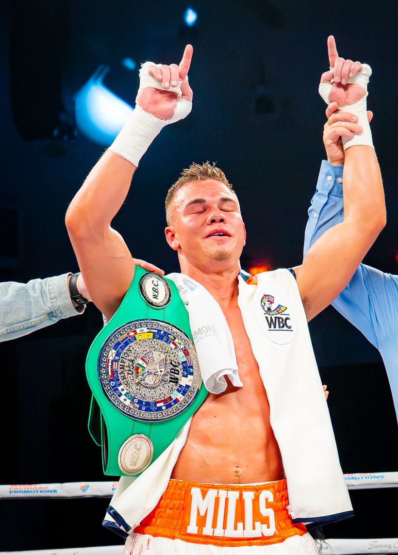 Champion with the belt on his shoulder and both hands up