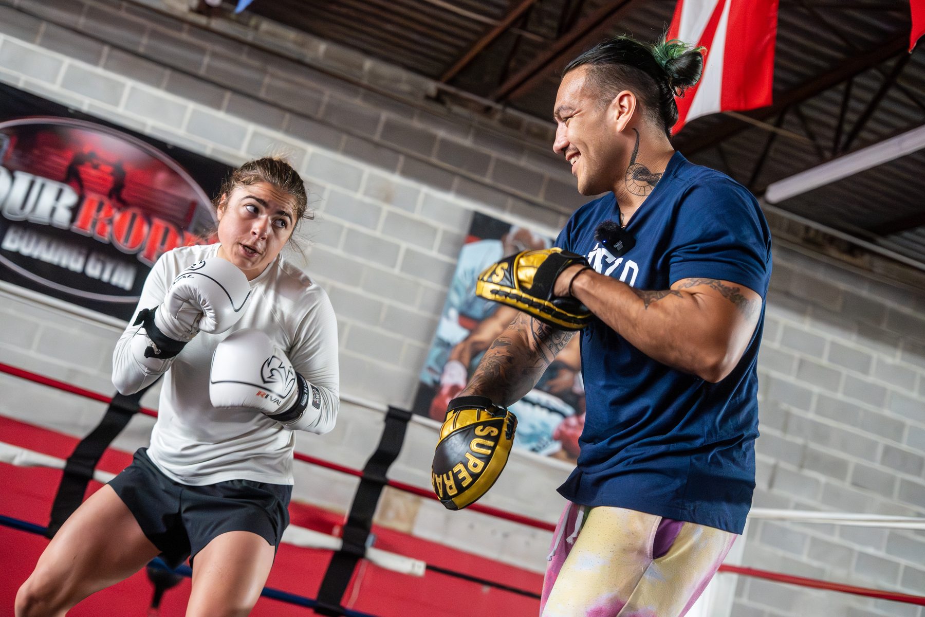 A coach holding pads for a fighter on the gym floor